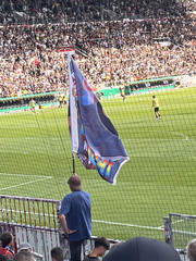 Fan mit einer Fahne im Fanblock FC Eintracht Noderstedt im Stadion am Millerntor gegen den FC St. Pauli bei einem Fußballspiel mit der Aktion Pfandbecherspende für das Diakonie Hospiz Norderstedt