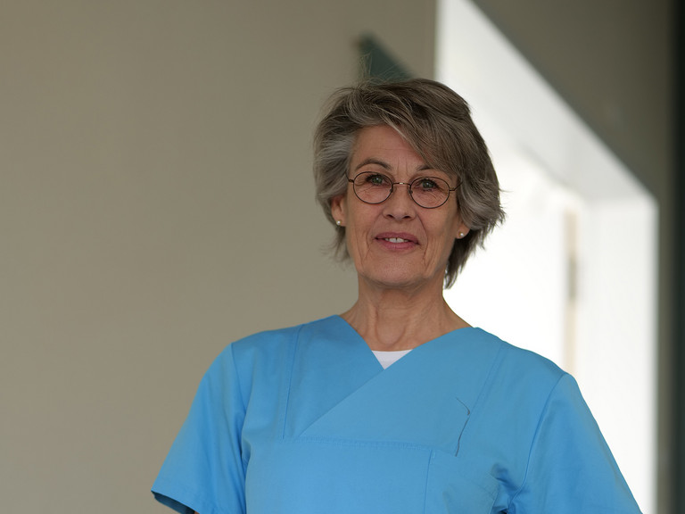 Stefanie Heldt, Leitung der Therapeutischen Dienste im Evangelischen Amalie Sieveking Krankenhaus, steht in blauer Arbeitskleidung in einem Klinikflur und blickt in die Kamera. Stefanie Heldt, Leitung der Therapeutischen Dienste im Evangelischen Amalie Sieveking Krankenhaus, steht in blauer Arbeitskleidung in einem Klinikflur und blickt in die Kamera.