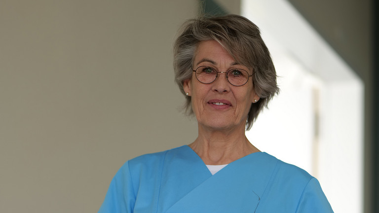 Stefanie Heldt, Leitung der Therapeutischen Dienste im Evangelischen Amalie Sieveking Krankenhaus, steht in blauer Arbeitskleidung in einem Klinikflur und blickt in die Kamera. Stefanie Heldt, Leitung der Therapeutischen Dienste im Evangelischen Amalie Sieveking Krankenhaus, steht in blauer Arbeitskleidung in einem Klinikflur und blickt in die Kamera.