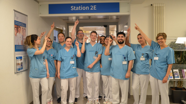 Gruppenfoto Auszubildende mit Stationsleitung und Ulrike Spiegel vor dem Stationseingang 2E im Amalie Sieveking Krankenhaus in Hamburg-Volksdorf