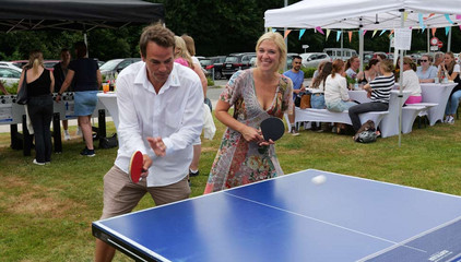 Ein Mann und eine Frau stehen mit Tischtennisschlägern auf einer Seite einer blauen Tischtennisplatte beim Sommerfest 2026 auf dem Gesundheitscampus Volksdorf vom Evangelischen Amalie Sieveking Krankenhaus, Residenz am Wiesenkamp, Feierabendhaus Volksdorf und Albertinen Kindertagesstätte Volksdorf. 