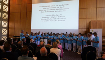 Mitarbeitende singen auf der Bühne im Chor bei der Verabschiedung Dr. Michael Musolf in den Ruhestand, Chefarzt der Klinik für Geriatrie und Physikalische Medizin im Evangelischen Amalie Sieveking Krankenhaus