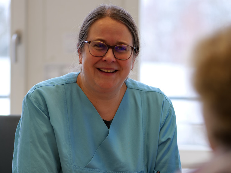 Dr. med. Saskia Otte, Chefärztin der Geriatrie & Physikalischen Medizin, sitzt an einem Schreibtisch in blauer Funktionskleidung und unterhält sich mit einer ihr gegenüber sitzenden Person im Amalie Sieveking Krankenhaus in Hamburg-Volksdorf Dr. med. Saskia Otte, Chefärztin der Geriatrie & Physikalischen Medizin, sitzt an einem Schreibtisch in blauer Funktionskleidung und unterhält sich mit einer ihr gegenüber sitzenden Person im Amalie Sieveking Krankenhaus in Hamburg-Volksdorf