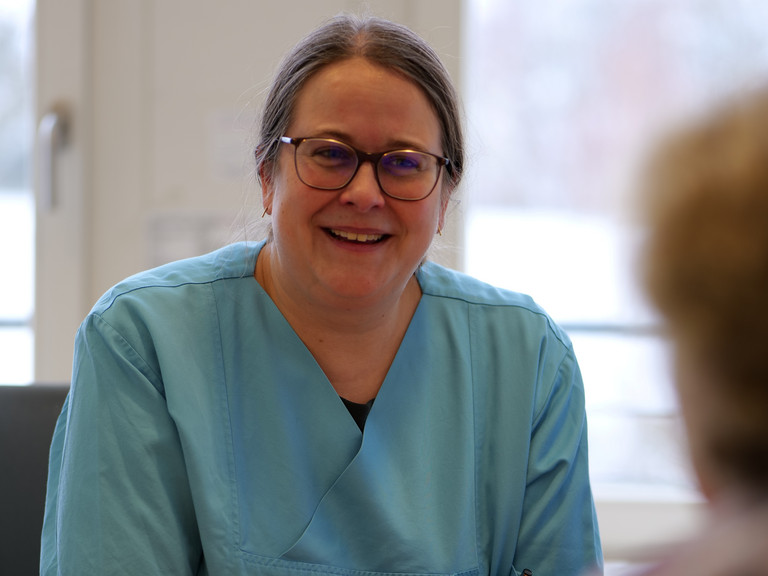 Dr. med. Saskia Otte, Chefärztin der Geriatrie & Physikalischen Medizin, sitzt an einem Schreibtisch in blauer Funktionskleidung und unterhält sich mit einer ihr gegenüber sitzenden Person im Amalie Sieveking Krankenhaus in Hamburg-Volksdorf Dr. med. Saskia Otte, Chefärztin der Geriatrie & Physikalischen Medizin, sitzt an einem Schreibtisch in blauer Funktionskleidung und unterhält sich mit einer ihr gegenüber sitzenden Person im Amalie Sieveking Krankenhaus in Hamburg-Volksdorf