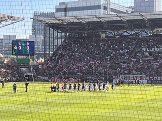 Einlauf von Spielern auf den Rasen im Stadion am Millerntor beim Spiel FC Eintracht Norderstedt gegen den FC St. Pauli mit Teil des Stadions im Hintergrund bei der Aktion Pfandbecherspende für das Diakonie Hospiz Norderstedt