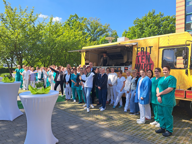 Eine große Gruppe von Pflegefachkräften steht vor einem Food Truck beim Immanuel Klinikum Bernau Herzzentrum Brandenburg und blickt in die Kamera beim Tag der Pflegenden