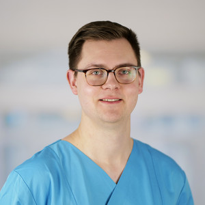 Portraitfoto von René Siebenborn, Pflegerischer Abteilungsleiter der Anästhesiologie und Intensivmedizin im Evangelischen Amalie Sieveking Krankenhaus in Hamburg, in blauer Funktionskleidung.