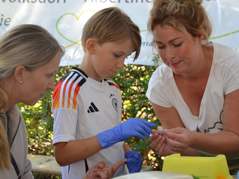 Ein Kind mit blauen Einmalhandschuhen bei einer Simulationsübung mit Mitarbeiterinnen an den Ständen des Gesundheitscampus Volksdorf der Immanuel Albertinen Diakonie beim Stadtteilfest Volksdorf in Hamburg