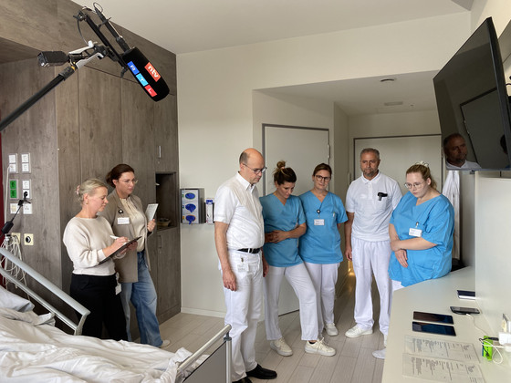Mitarbeitende, Pflegekräfte und der Ärztliche Direktor Prof. Dr. med. Ernst von Dobschütz stehen in einem Patientenzimmer und diskutiert einen Fall bei der Übung Room of Horrors mit TV-Begleitung im Amalie Sieveking Krankenhaus in Hamburg-Volksdorf