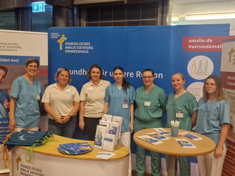 Sieben Mitarbeiterinnen der Hamburger Einrichtungen der Immanujel Albertinen Diakonie stehen nebeneinander an einem Stand auf der Berufsorientierungsmesse
