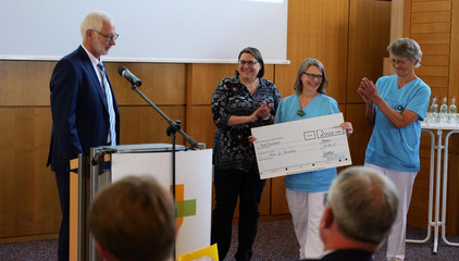 Übergabe eines Spendenscheck auf der Bühne mit Dr. Michael Musolf bei dessen Verabschiedung in den Ruhestand, Chefarzt der Klinik für Geriatrie und Physikalische Medizin im Evangelischen Amalie Sieveking Krankenhaus
