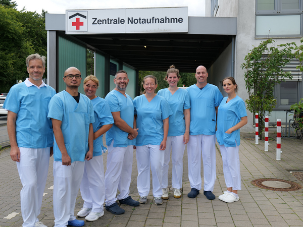 Das Team der Zentralen Notaufnahme im Evangelischen Amalie Sieveking Krankenhaus in Hamburg steht in Dienstkleidung vor dem Eingang