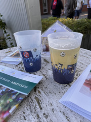 Zwei Plastikbecher und Infobroschüren auf dem Tisch am Infostand des Hospizes bei einem Fußballspiel des FC Eintracht Norderstedt vor dem Stadion bei der Aktion Pfandbecherspende für das Diakonie Hospiz Norderstedt