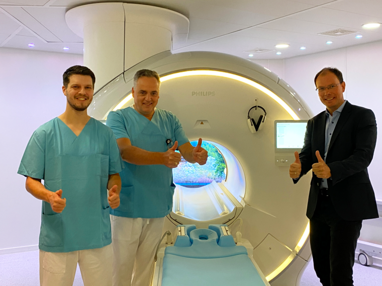 R. Grundherr, Leitender Medizinischer Technologe, Prof. Dr. C. Weber, Chefarzt und Leiter des Immanuel Albertinen Zentrums für Radiologie, und Geschäftsführer Andreas Schneider stehen vor dem neuen MRT-Gerät, blicken in die Kamera und halten die Daumen hoch