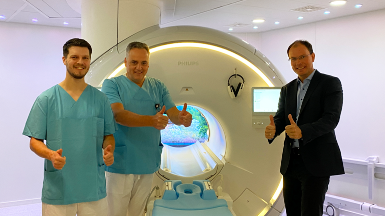 R. Grundherr, Leitender Medizinischer Technologe, Prof. Dr. C. Weber, Chefarzt und Leiter des Immanuel Albertinen Zentrums für Radiologie, und Geschäftsführer Andreas Schneider stehen vor dem neuen MRT-Gerät, blicken in die Kamera und halten die Daumen hoch