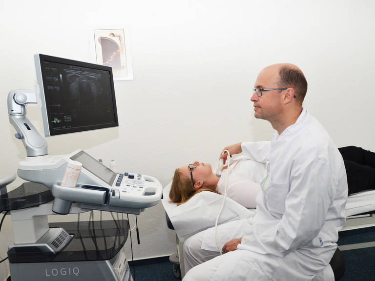 Arzt untersucht eine Patientin auf einer Liege mit Ultraschall am Hals - Evangelisches Amalie Sieveking Krankenhaus Hamburg - Schilddrüsenknoten Behandlung