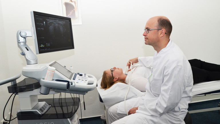 Arzt untersucht eine Patientin auf einer Liege mit Ultraschall am Hals - Evangelisches Amalie Sieveking Krankenhaus Hamburg - Schilddrüsenknoten Behandlung