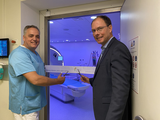 Prof. Dr. Weber, Chefarzt und Leiter des Immanuel Albertinen Zentrums für Radiologie, und Geschäftsführer A. Schneider stehen vor dem blau erleuchteten Raum mit dem neuen MRT-System im Amalie Sieveking Krankenhaus in Hamburg und schneiden das Band zur Eröffnung durch