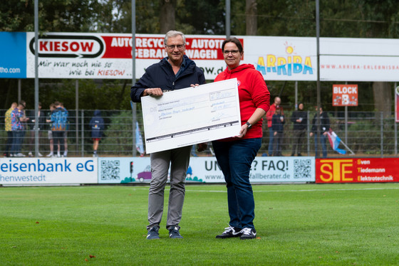 Jens Klindworth (l.), Einrichtungsleiter & Pflegedienstleiter, und die Vereinsverantwortliche mit einem übergroßen Spendenscheck von der Becherpfandaktion FC Eintracht Norderstedt für das Albertinen Hospiz Norderstedt im Stadion