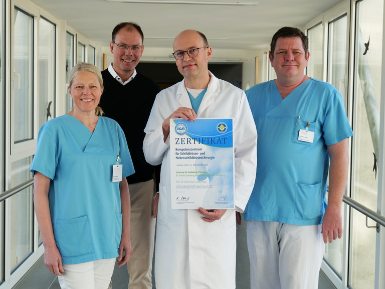 Vier Mitarbeitende des Evangelischen Amalie Sieveking Krankenhauses stehen nebeneinander und präsentieren die DGAV-Zertifizierung für das Zentrum für Endokrine Chirurgie: Dr. Denise Wittek, Geschäftsführer Andreas Schneider, Prof. Dr. Ernst von Dobschütz und Oberarzt Alexander Gnoss. Vier Mitarbeitende des Evangelischen Amalie Sieveking Krankenhauses stehen nebeneinander und präsentieren die DGAV-Zertifizierung für das Zentrum für Endokrine Chirurgie: Dr. Denise Wittek, Geschäftsführer Andreas Schneider, Prof. Dr. Ernst von Dobschütz und Oberarzt Alexander Gnoss.