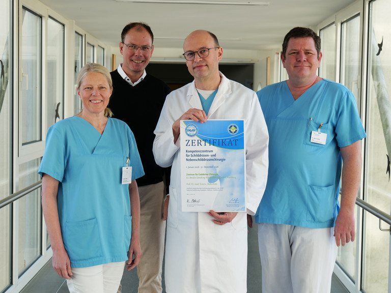 Vier Mitarbeitende des Evangelischen Amalie Sieveking Krankenhauses stehen nebeneinander und präsentieren die DGAV-Zertifizierung für das Zentrum für Endokrine Chirurgie: Dr. Denise Wittek, Geschäftsführer Andreas Schneider, Prof. Dr. Ernst von Dobschütz und Oberarzt Alexander Gnoss.