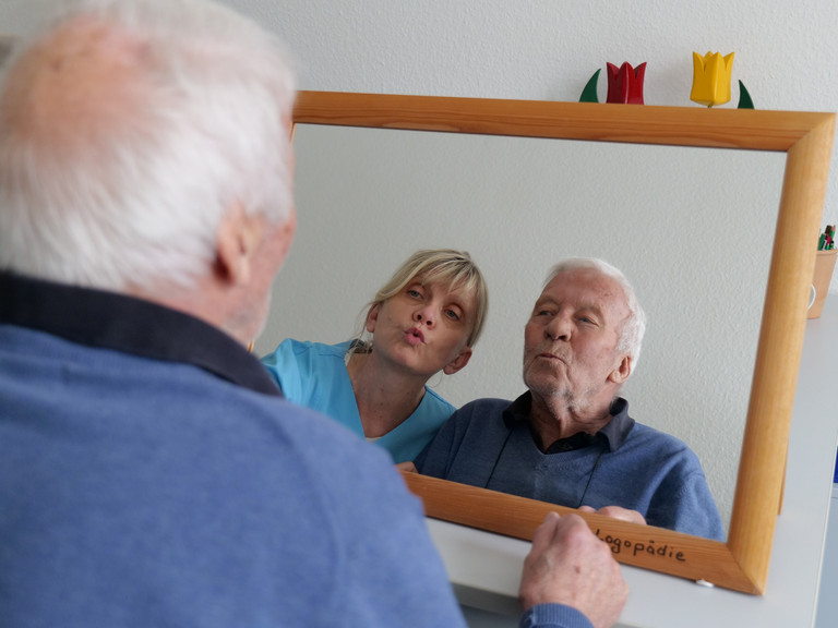 Ein Patient der Geriatrie & Physikalischen Medizin blickt gemeinsam mit einer Therapeutin in blauer Funktionskleidung in einen Spiegel während der logopädischen Therapie im Amalie Sieveking Krankenhaus in Hamburg-Volksdorf Ein Patient der Geriatrie & Physikalischen Medizin blickt gemeinsam mit einer Therapeutin in blauer Funktionskleidung in einen Spiegel während der logopädischen Therapie im Amalie Sieveking Krankenhaus in Hamburg-Volksdorf