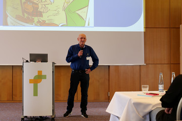 Ein Arzt in Alltagskleidung steht mit einem Mikrofon auf dem Podium vor einer Leinwand neben einem Sprechpult und hält einen Vortrag bei der Fachveranstaltung 11. Amalie Tag der Hausärztinnen und Hausärzte im Evangelischen Amalie Sieveking Krankenhaus in Hamburg-Volksdorf.